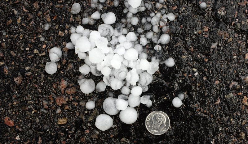 Hailstones of various sizes next to a dime for scale on dark ground