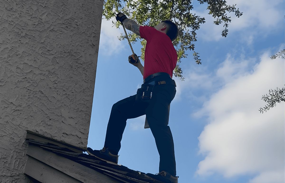 RainTech technician in a red shirt checking a roof edge from a ladder