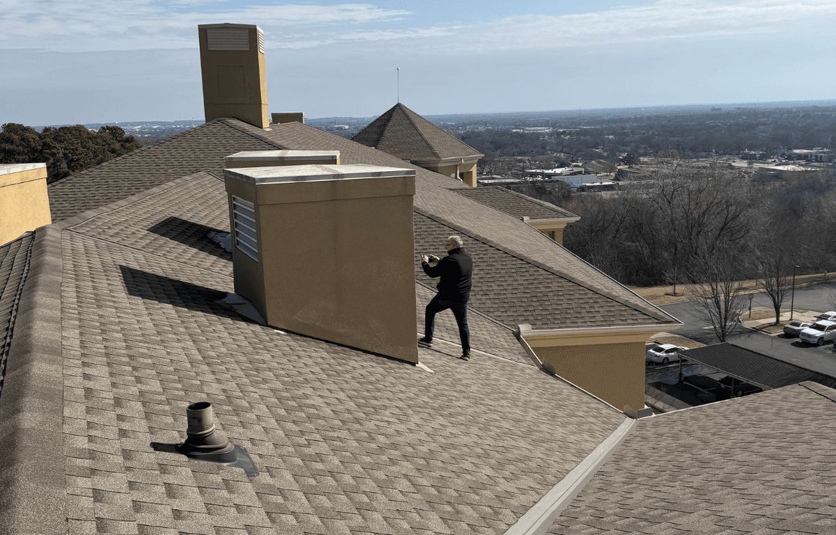Roofer walking a large shingle roof with chimneys above a Tulsa neighborhood