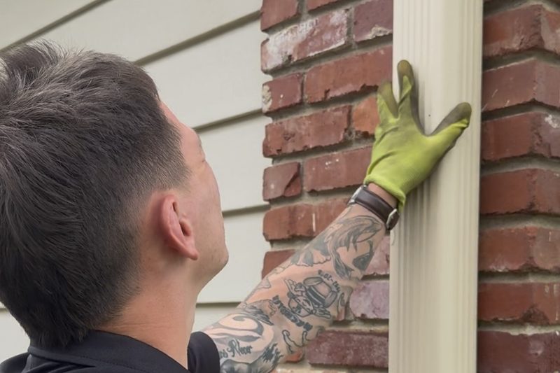 RainTech inspector checking a downspout for hail dents during a storm inspection