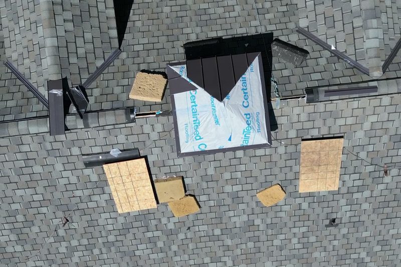Aerial view of a shingle roof mid-repair, with decking patches and new underlayment around a dormer