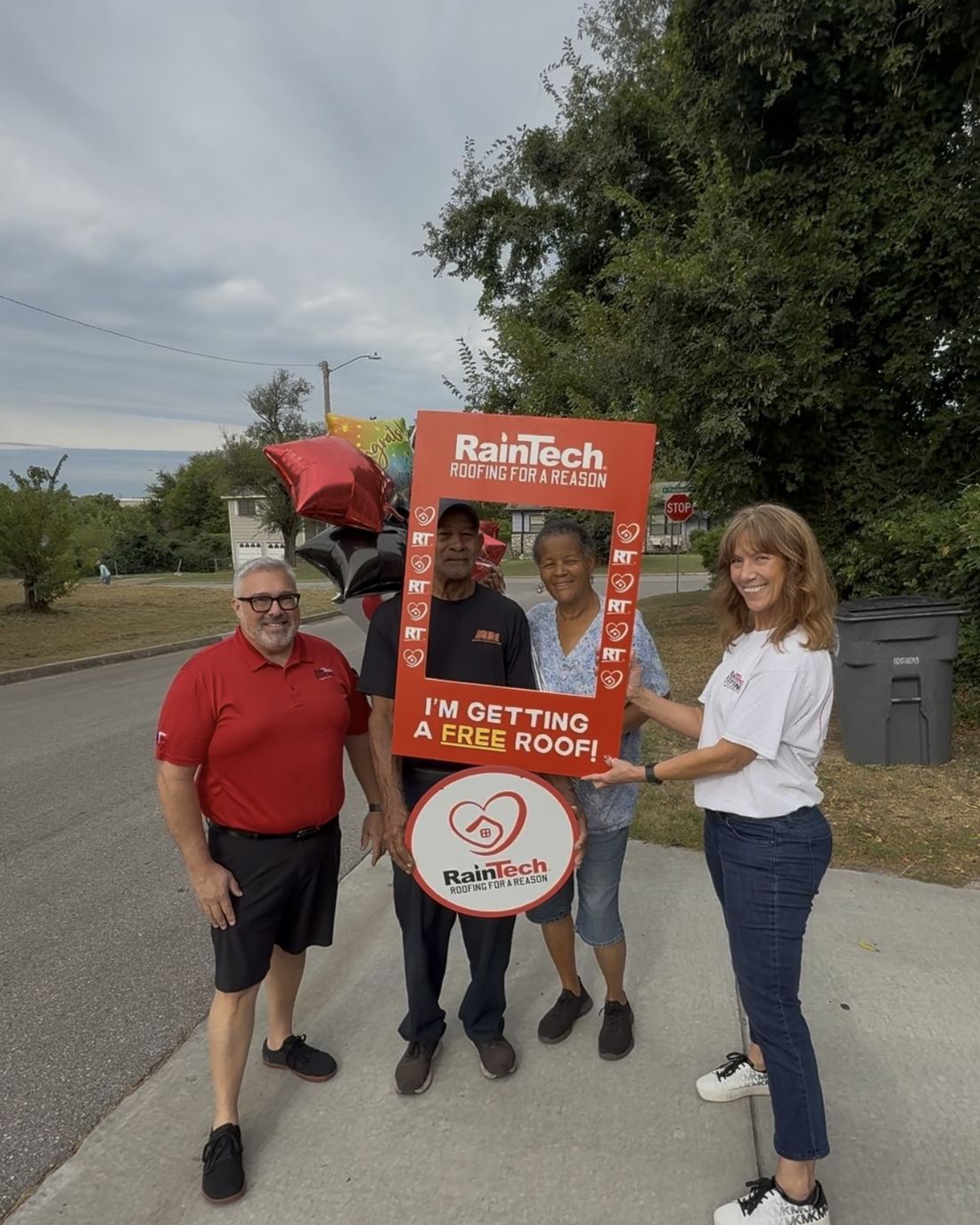 A Roofing for a Reason recipient holding an 'I'm getting a free roof' sign with the RainTech team