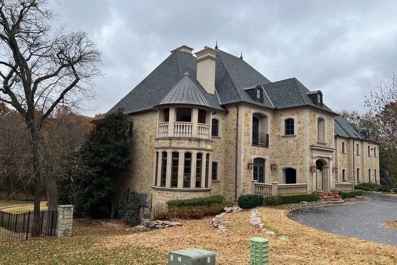 Stone estate home in Wenmoor Estates with a dark shingle roof and turret