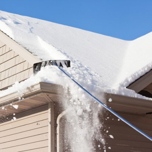 Winter Roof Maintenance: Homeowner Clearing Snow off a Roof.